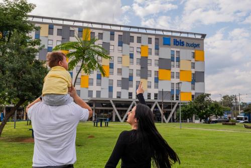 a man holding a child on his shoulders in front of a building at Ibis Budget Guarulhos Aeroporto in Guarulhos