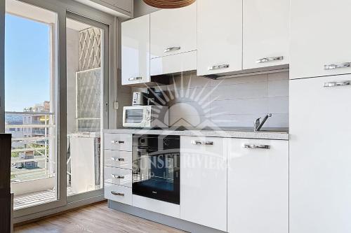 d'une cuisine avec des placards blancs, un four micro-ondes et une fenêtre. dans l'établissement L'AIGLON Appartement AirCo in the town center for 4 By Sunset, à Antibes