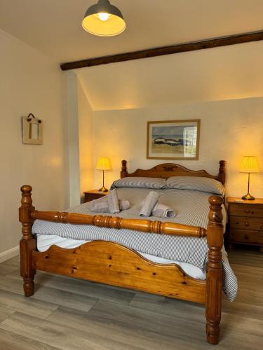 a large wooden bed in a bedroom with two lamps at Titmouse at Trenale Court Cottages in Tintagel