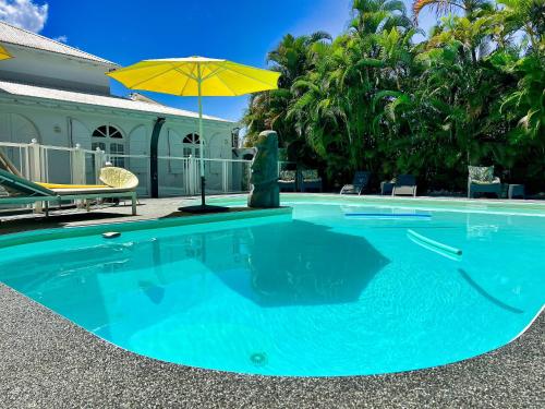 a swimming pool with an umbrella next to a house at GREEN LORD DOMAINE - Lodges Piscine & Spa - Bar & Lounge - Restaurant gastronomique in Lamentin