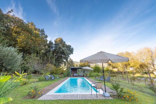 a swimming pool with an umbrella and chairs and a house at Nature Escape with Pool & BBQ in Viana do Castelo