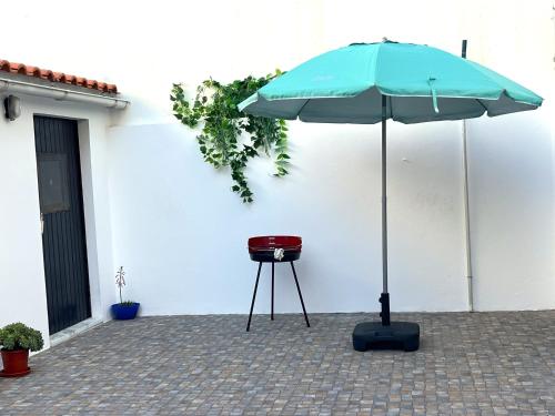 a grill and an umbrella next to a white wall at CASA DAS MARÉS MILFONTES by Stay in Alentejo in Vila Nova de Milfontes