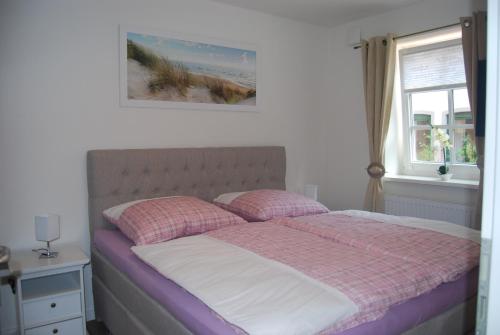 ein Bett mit rosa und weißer Bettwäsche und einem Fenster in der Unterkunft Haus Adria in Schleswig