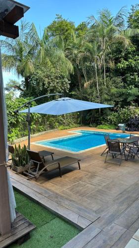 a patio with a blue umbrella and chairs and a pool at Grey House in Foz do Iguaçu
