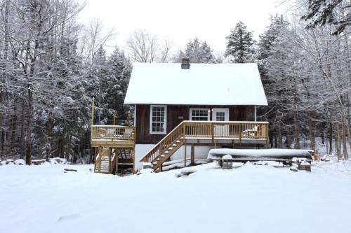 a log cabin with a deck in the snow at Dream Stratton Forest Cabin with Hot Tub and Fast WiFi in Stratton