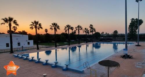 a large pool with palm trees and a sunset in the background at Campinho house in Campinho