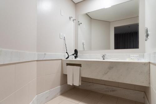 a white bathroom with a sink and a mirror at Jk Premium Hotel e Eventos in Londrina