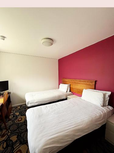 two beds in a hotel room with a pink wall at Simplystay Lincoln Road in Skegness