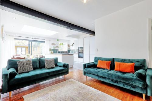 a living room with two green couches and orange pillows at Beautiful 5 bed house, relaxing garden and driveway parking 10 min to the beach in Southend-on-Sea