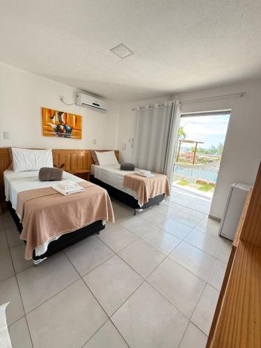a hotel room with two beds and a large window at Milano Hotel Pousada Canoa Quebrada in Canoa Quebrada