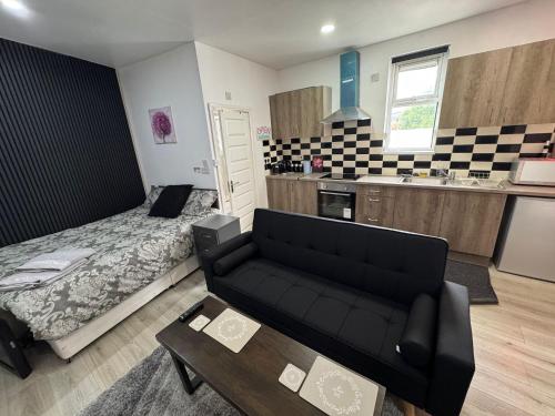 a living room with a black couch and a kitchen at Self-Contained Studio with kitchen & bathroom - Warm Welcome Inn , Stirchley in Birmingham