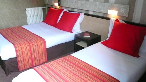two beds with red pillows in a hotel room at Hôtel L'Européen in Tarbes