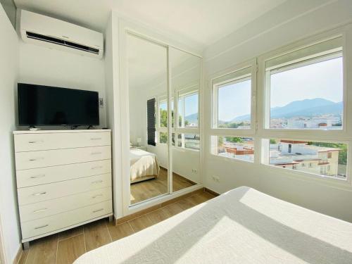 sypialnia z komodą z telewizorem i oknami w obiekcie Luminoso ático con vistas al mar en Torremolinos w mieście Torremolinos