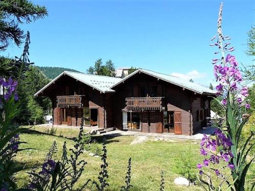 une grande maison en bois dans un champ avec des fleurs violettes dans l'établissement CASA-Forêt Blanche splendid chalet 13p, à Risoul