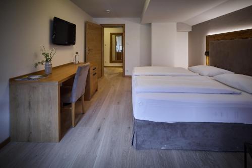 a room with two beds and a desk and a television at Designhotel Sonnhof by Vitus Winkler in Sankt Veit im Pongau