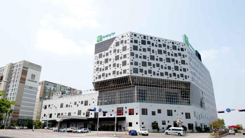 a tall building with cars parked in a parking lot at Holiday Inn Gwangju by IHG in Gwangju