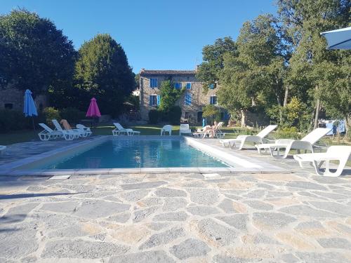 une piscine avec des chaises longues blanches et une maison dans l'établissement grand gîte de charme en Cévennes, à Fressac