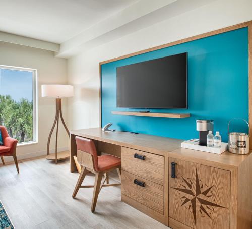 a room with a desk with a television on a blue wall at Compass by Margaritaville Flagler Beach in Flagler Beach
