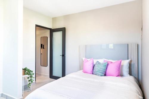 um quarto branco com almofadas rosa e azuis em uma cama em Fully Renovated Beachside with Oceanview 1 Bedroom Unit 7 em Dorado