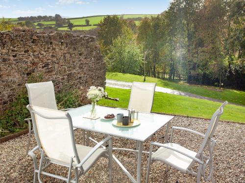 a table and chairs on a gravel patio with a stone wall at Uk45542-The Farm House in Sticklepath