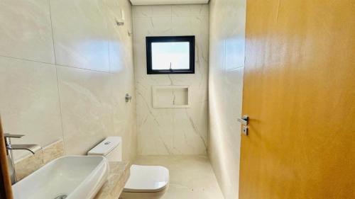 a bathroom with a toilet and a sink and a window at Casa para família com piscina in Guarujá