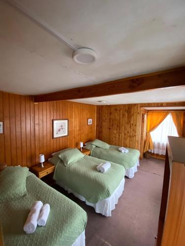 three beds in a room with wooden walls at Hotel Elizabeth in Coñaripe