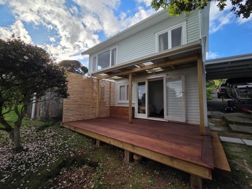 a house with a wooden deck in the yard at Classic bach near the beach in Oneroa