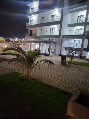 a tall building with a palm tree in front of it at Melias Hotel Diamniadio in Dogar
