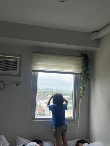 a young child is looking out of a window at Cozy 2BR Stay for 6pax in High-Floor, Wi-Fi & Family Games near IT Park Cebu- Unit Scarlett by GERRA in Mandaue City