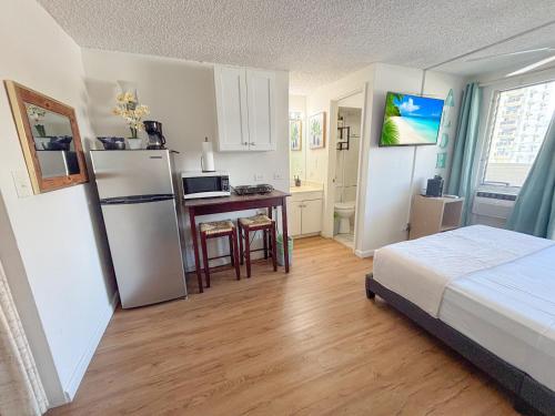 a bedroom with a bed and a kitchen with a refrigerator at Mellow Kuhio Village Studio condo in Honolulu