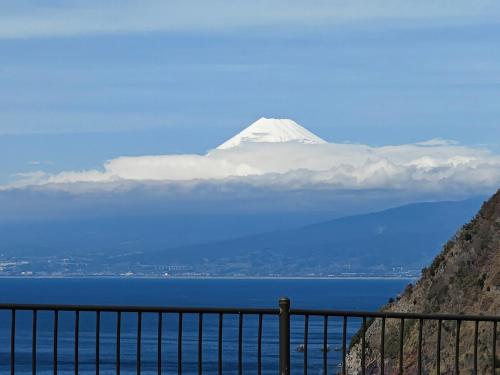 a snow capped mountain in the distance with the ocean and a fence at 貸切宿 ひととき -Hitotoki- 眺めの良いテラスでBBQが楽しめる 徒歩で海と温泉へ 温泉券プレゼント 最大12名 in Numazu