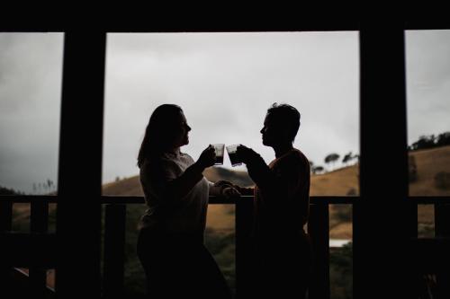 a man and a woman drinking coffee in front of a window at Chale com hidro na Serra da Mantiqueira in Sapucaí-Mirim