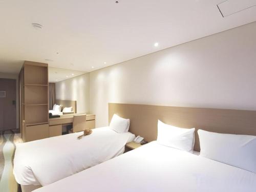 two beds in a hotel room with white sheets at Ebenezer Hotel in Jeju