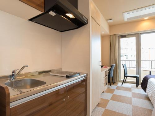 a kitchen with a sink and a bed with a window at Community & Spa Naha Central Hotel in Naha