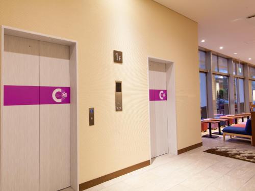 a row of elevators in an office lobby with tables at Community & Spa Naha Central Hotel in Naha
