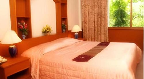 a bedroom with a bed with two lamps and a window at Pailyn Hotel in Sukhothai