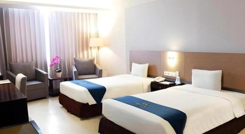 a hotel room with two beds and a chair at Grage Hotel Cirebon in Cirebon