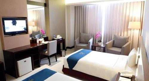 a hotel room with a bed and a desk and a television at Grage Hotel Cirebon in Cirebon