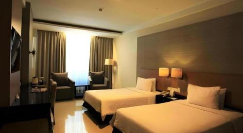 a hotel room with two beds and a chair at Grage Hotel Cirebon in Cirebon