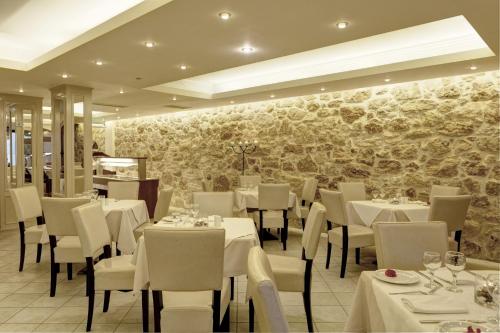 a restaurant with white tables and chairs and a stone wall at Indigo Mare in Plataniás