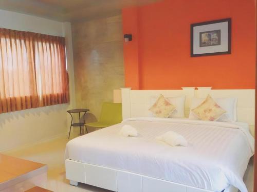 a bedroom with a white bed with an orange wall at Waenpetch place Hotel in Ubon Ratchathani