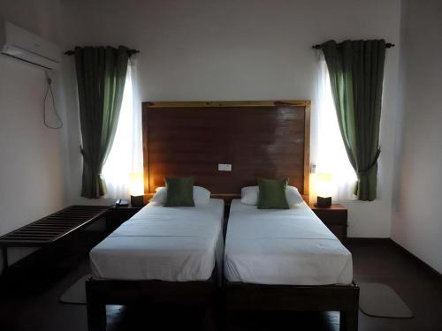 two beds in a hotel room with green curtains at Naaval Hotel in Batticaloa