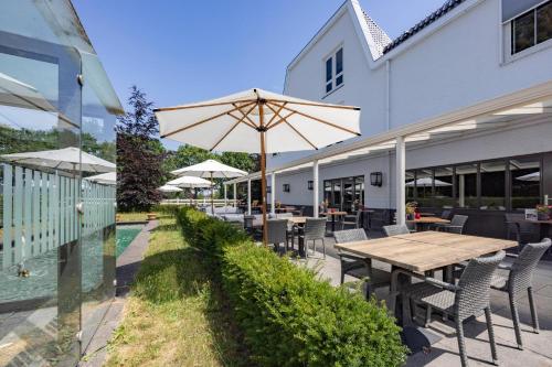 a patio with a wooden table and chairs and an umbrella at Fletcher Hotel-Restaurant Het Witte Huis in Amersfoort