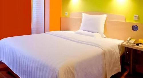 a bedroom with a large white bed with an orange wall at 7 Days Inn Hohhot University East Street in Hohhot