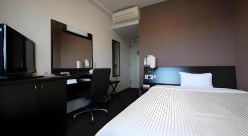 a bedroom with a bed and a desk and a tv at Hotel Route Inn Furukawa Ekimae in Osaki