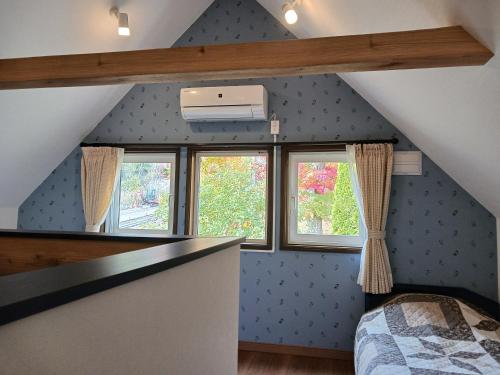 a attic room with a bed and two windows at Cottage Morino Nakamatachi in Furano