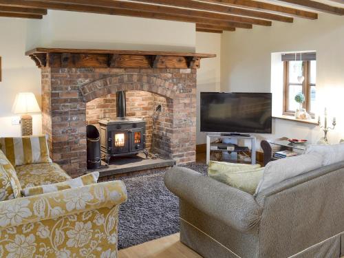 a living room with a brick fireplace and a television at Buddileigh Farm in Betley