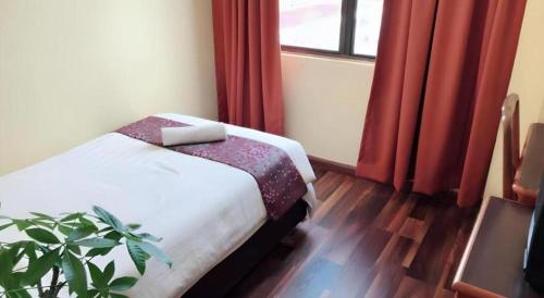 a bedroom with a bed with red curtains and a plant at Global Hotel Labuan in Labuan