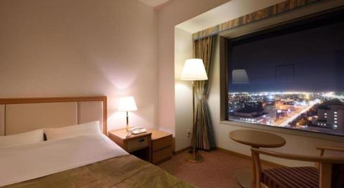 a bedroom with a large window with a view of a city at Grand Hotel New Oji in Tomakomai