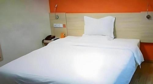 a large white bed in a bedroom with an orange wall at 7 Days Inn Siping Xinhua Street in Siping